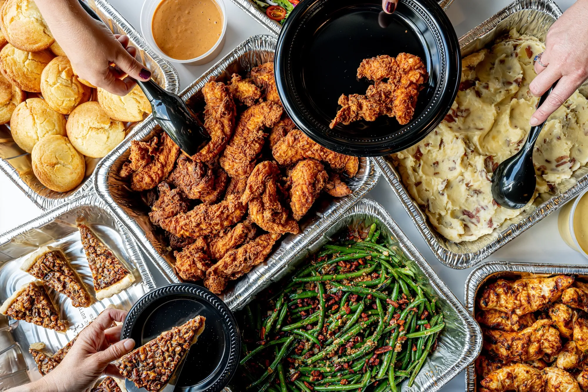 A full table of food including chicken tenders, potatoes, green beans, bread, and pecan pie